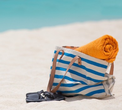 blue striped beach bag with orange towel and flip-flops on beach | Coastline Realty Vacations