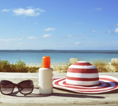 red striped hat, sunglasses and sunscreen on beach | Coastline Realty Vacations