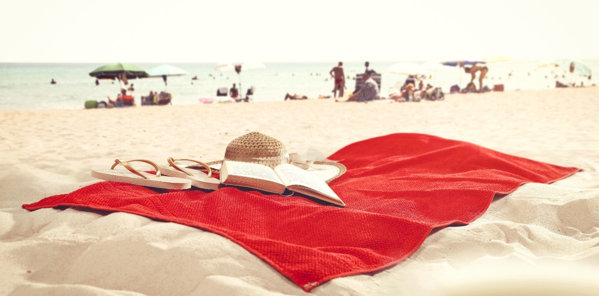 red towel with book, flip flops and beach hat on beach | Coastline Realty Vacations