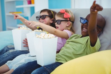 three children watching a movie and eating popcorn | Coastline Realty