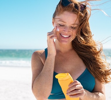 woman applying sunscreen on the beach | Coastline Realty
