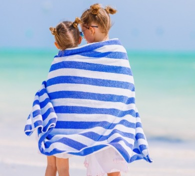 little girls wrapped up in beach towel on the beach | Coastline Realty