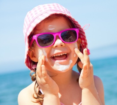 little girl wearing sun hat, sunglasses, and sunscreen on the beach | Coastline Realty