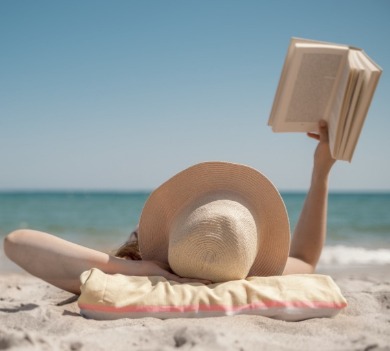 woman laying on the beach reading a book | Coastline Realty