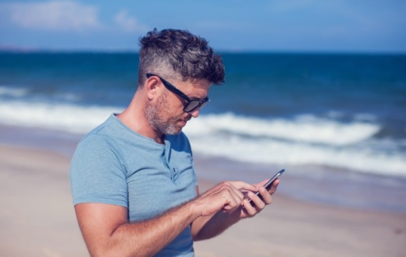man using cell phone on the beach | Coastline Realty
